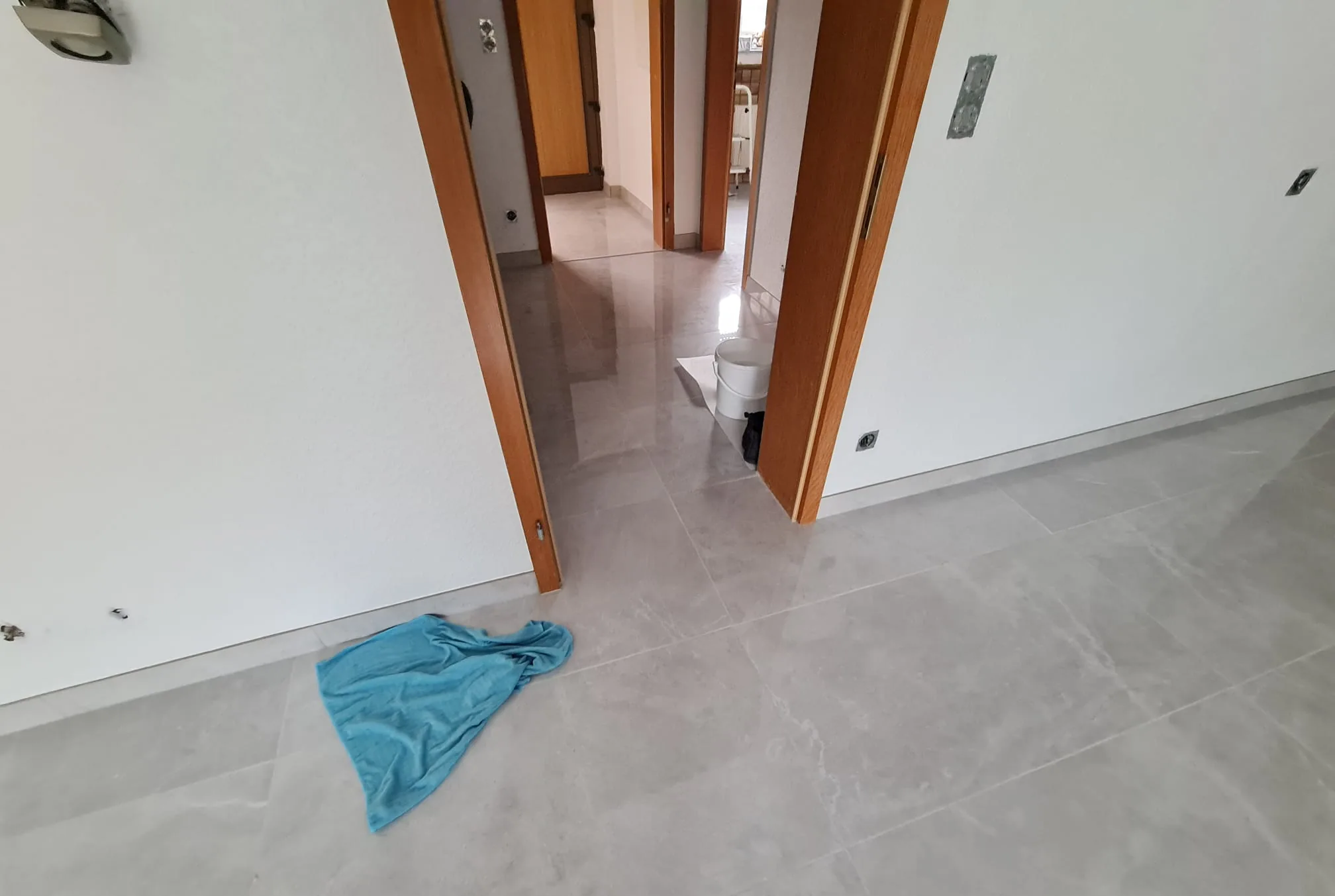 Fertig renovierter Flur — glänzender Großformat-Fliesenboden, weiß gestrichene Wände und warme Holzzargen
