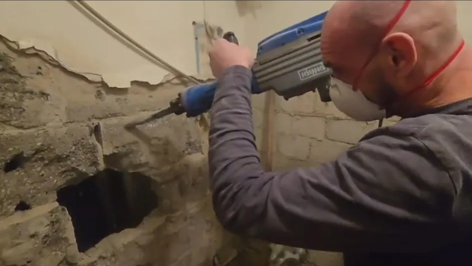Adrian Polaczek stemmt mit Stemmhammer und Staubmaske eine Wand auf