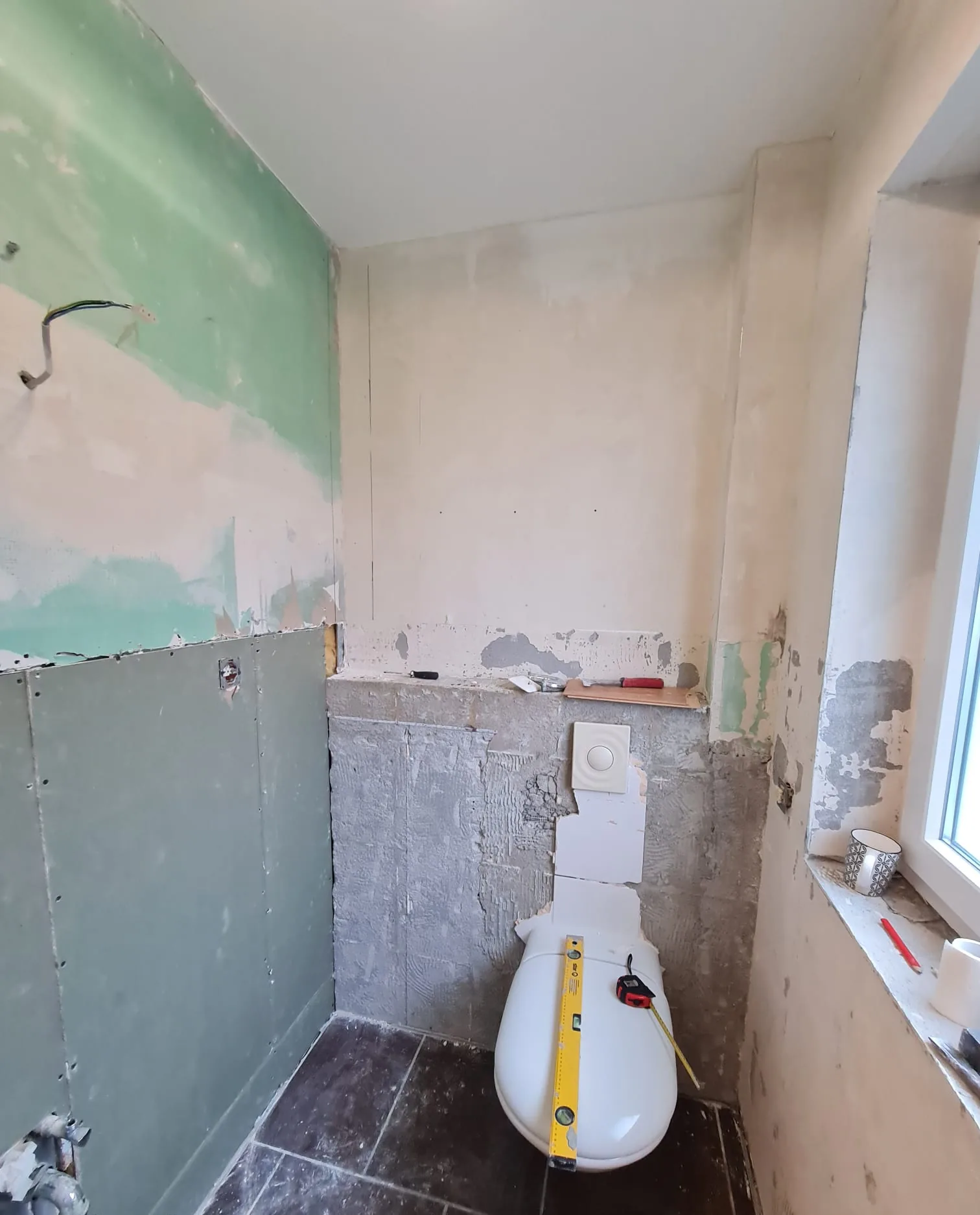 Dasselbe Bad während der Sanierung — WC-Vorwand im Rohbau, dunkler Fliesenboden bereits verlegt
